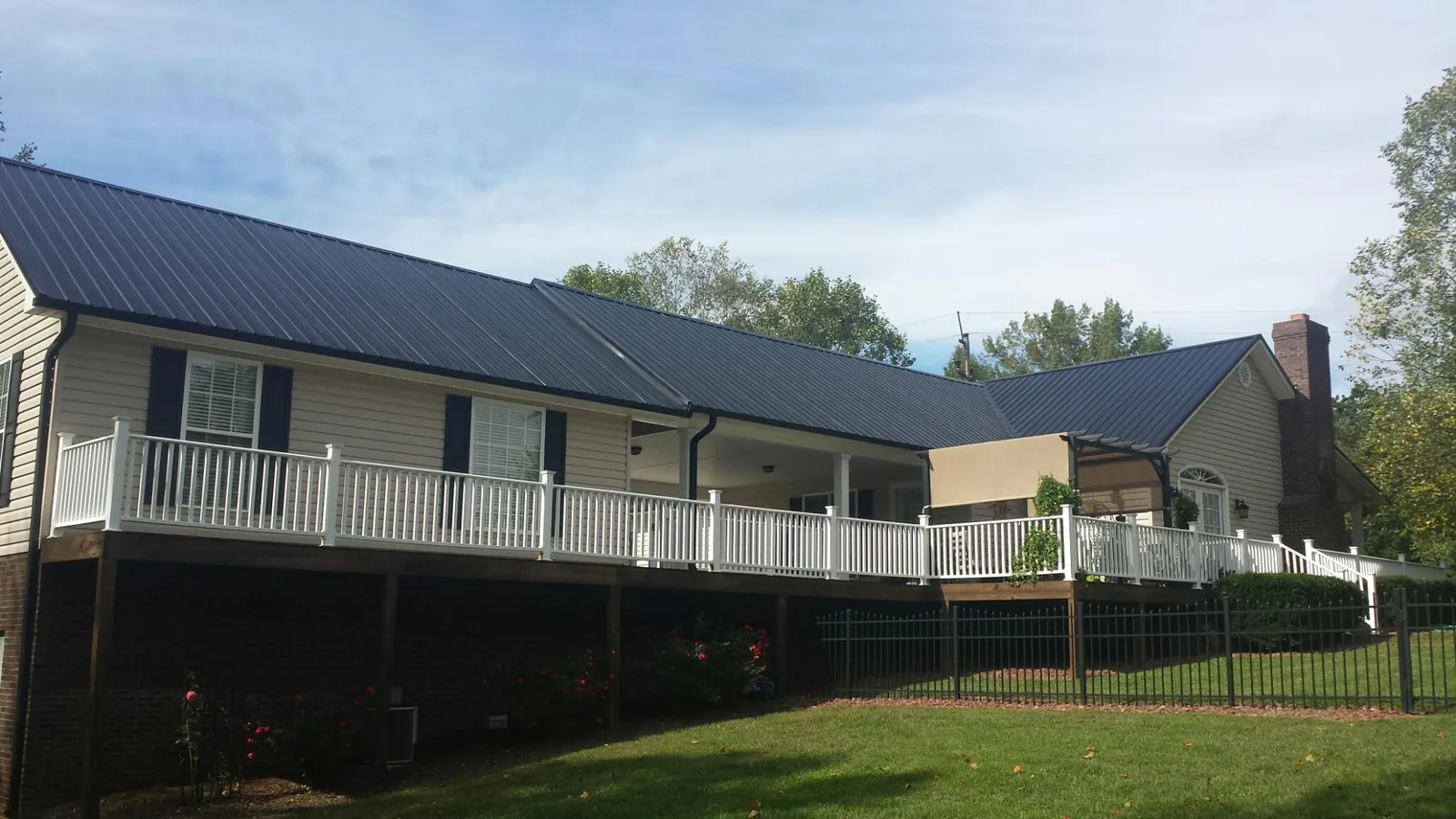 Black metal roof above a long white railed deck on a hillside home in Blair