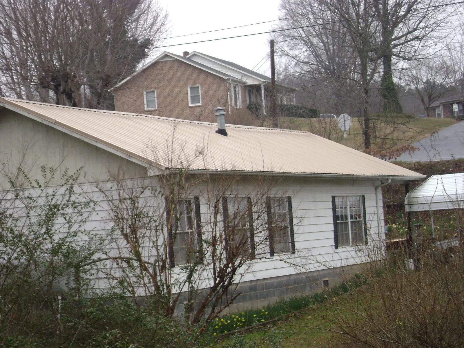 Tan metal roof on a white sided house set into a hillside — Commercial Roofing by Roofing Brothers in Blair